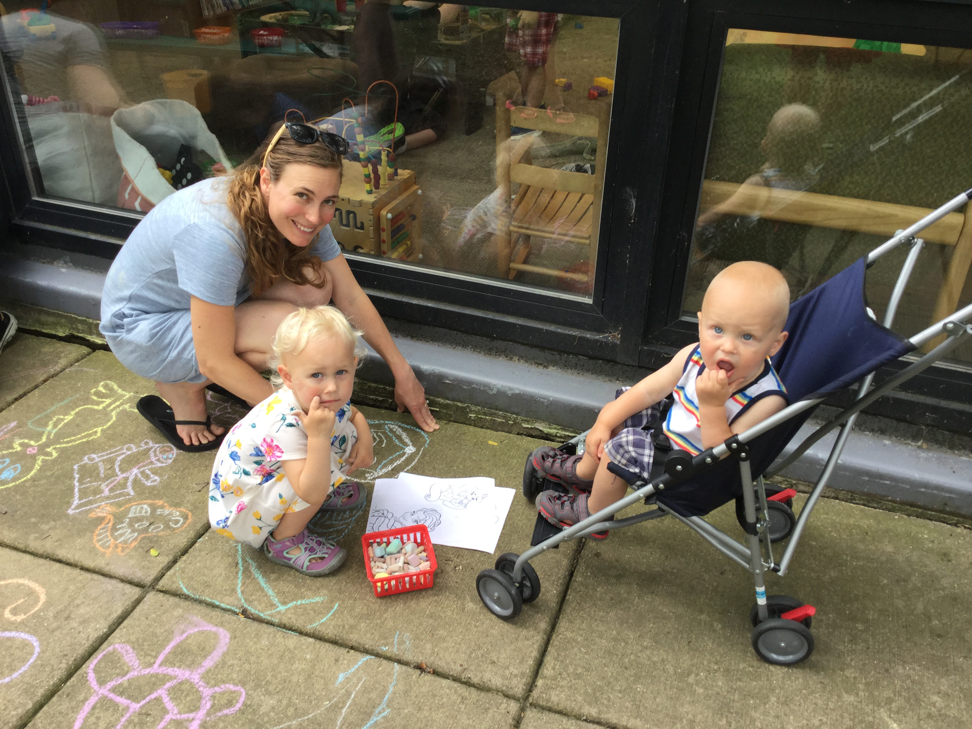Chalk the Walk event photo showing a woman and two babies drawing with chalk on sidewalk
