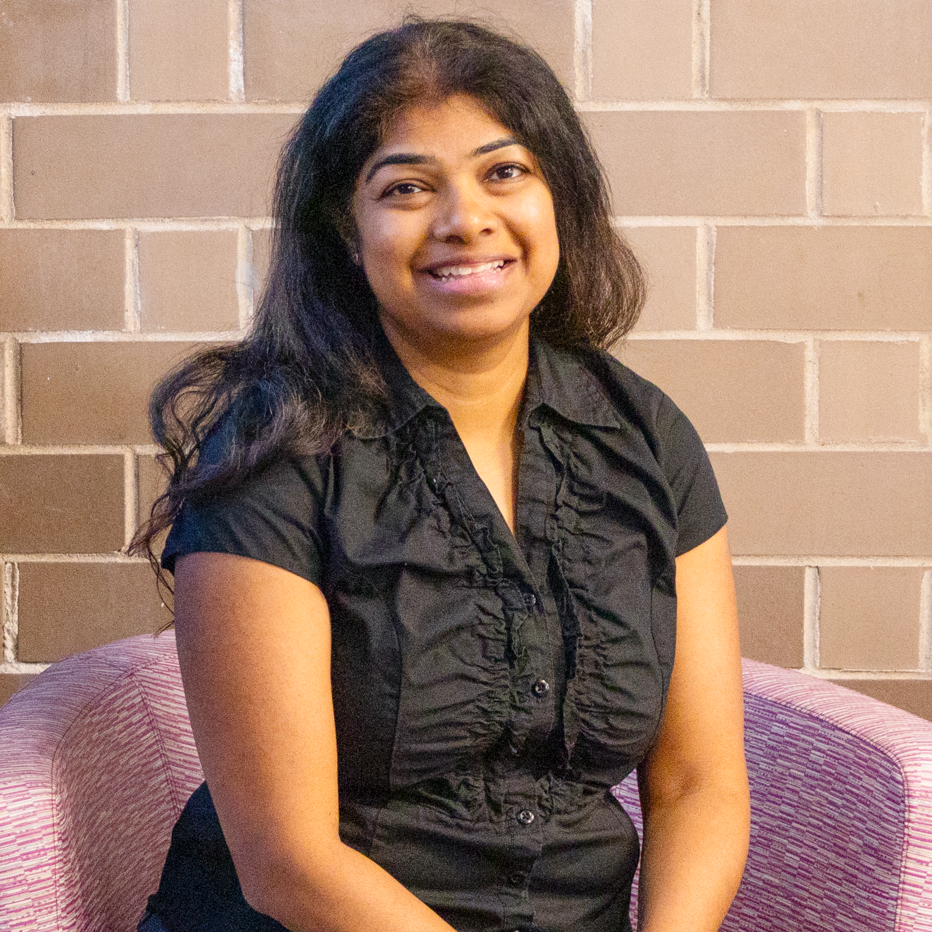 Photo of Sandhya Patel our Board Treasurer sitting in a chair smiling at the camera.