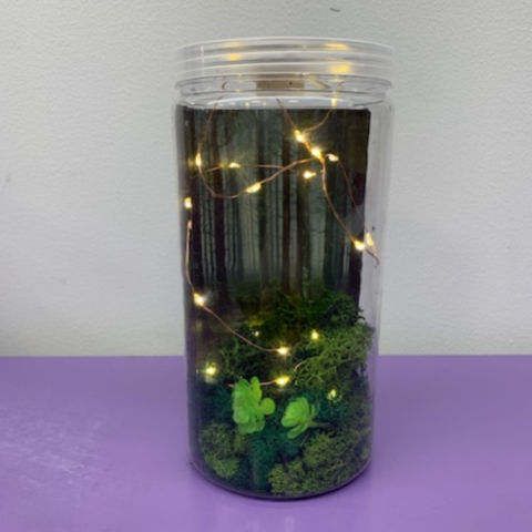 a picture of a jar with a forest and fairy lights inside against a white and purple background