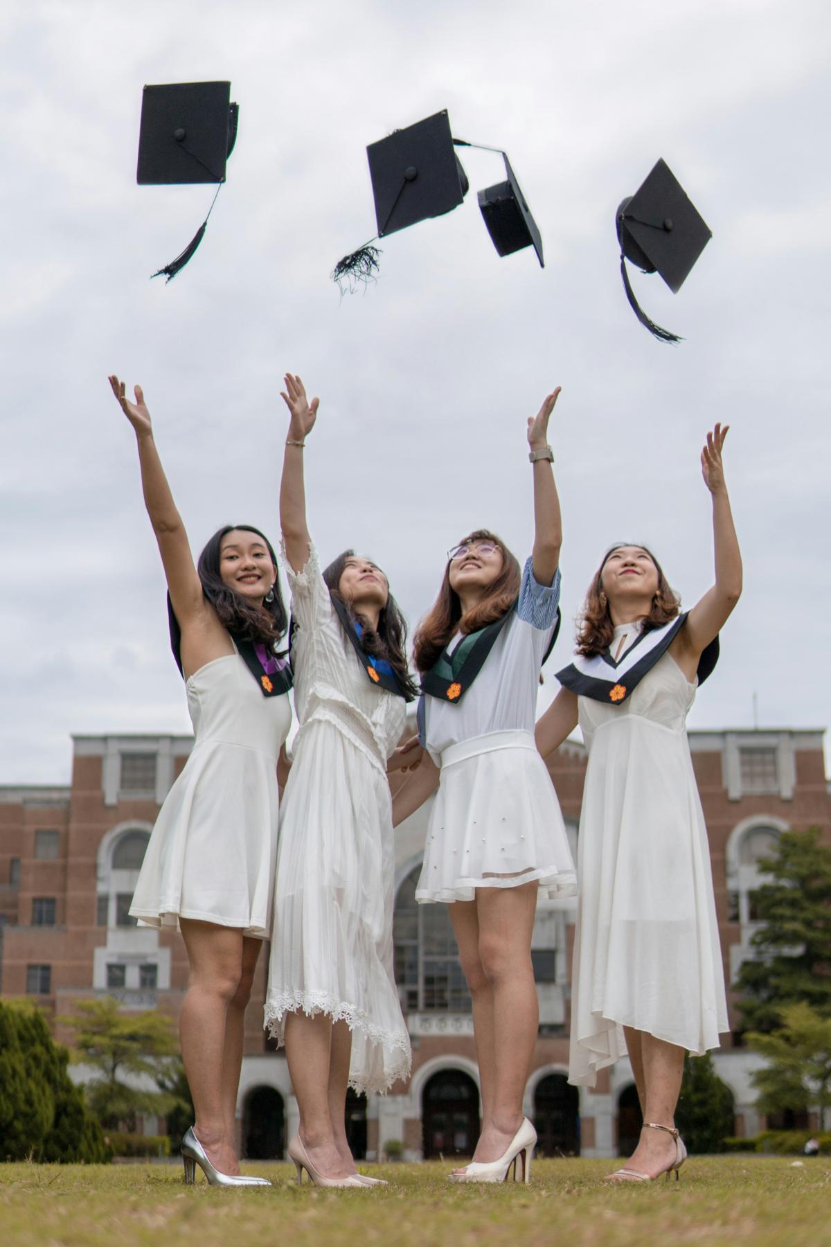 four woman throwing graduation caps in the air outside