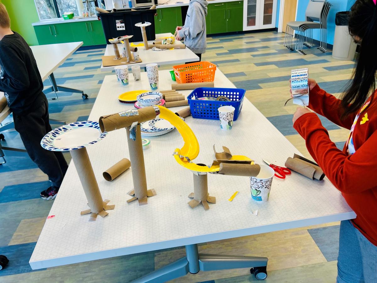 Kids building a rollercoaster out of paper rolls and tape.